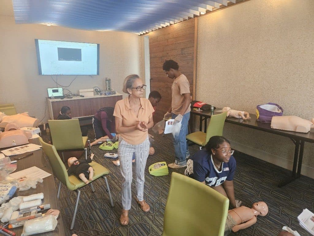 An instructor leads a CPR and First Aid practice with training manikins and an AED trainer